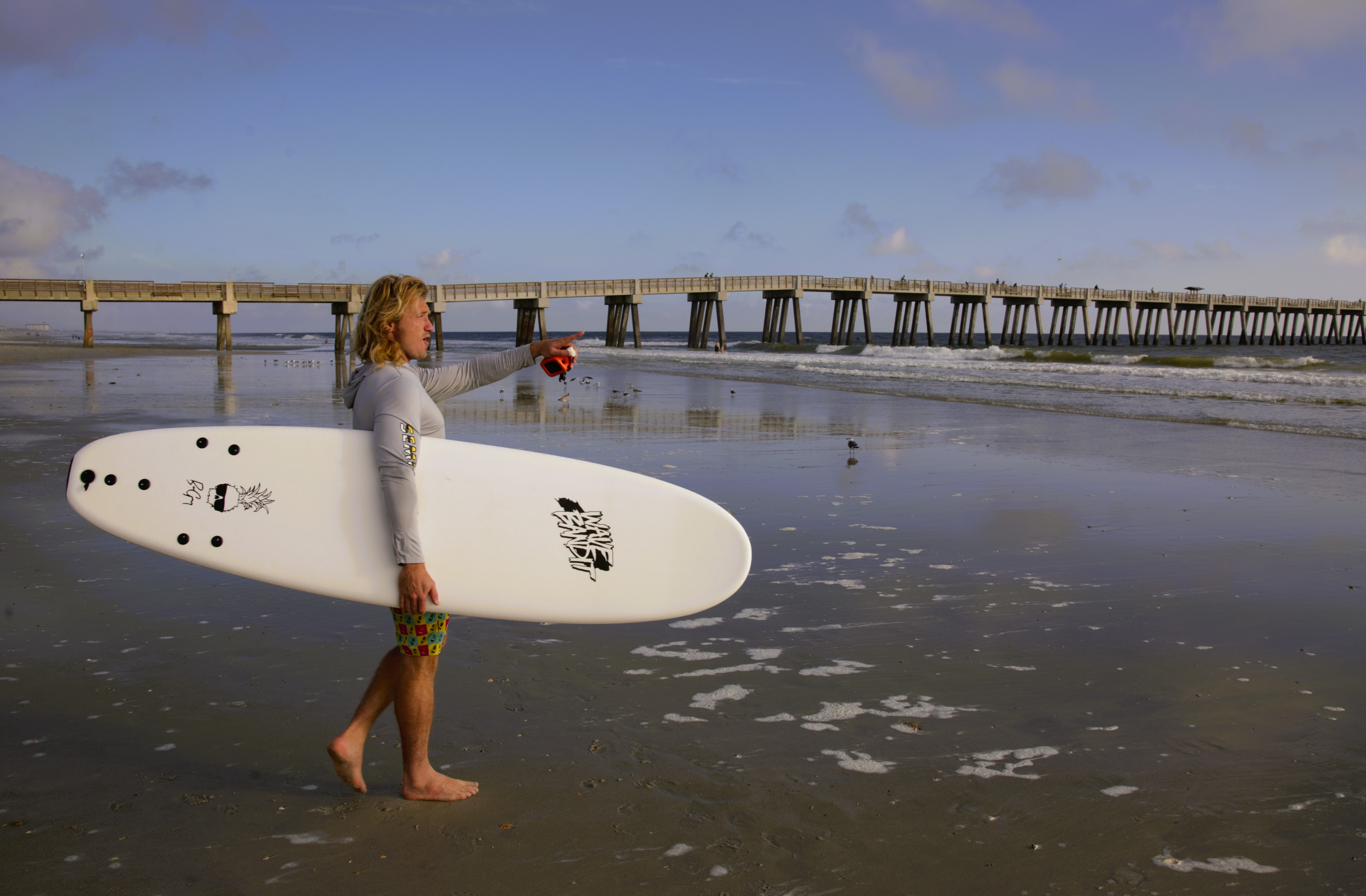 Ben Gravy on the sand pointing, Catch Surf board and GoPro, Jacksonville pier behind.