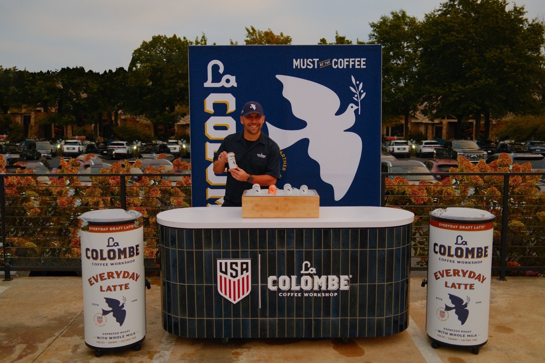 La Colombe brand ambassador at the retail bar with branded coolers and SEG backdrop.